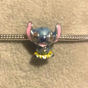 May include: A blue and pink Stitch charm bead with a yellow and white collar on a silver bracelet. This charm is a collectible item, ideal for fans of the animated movie.
