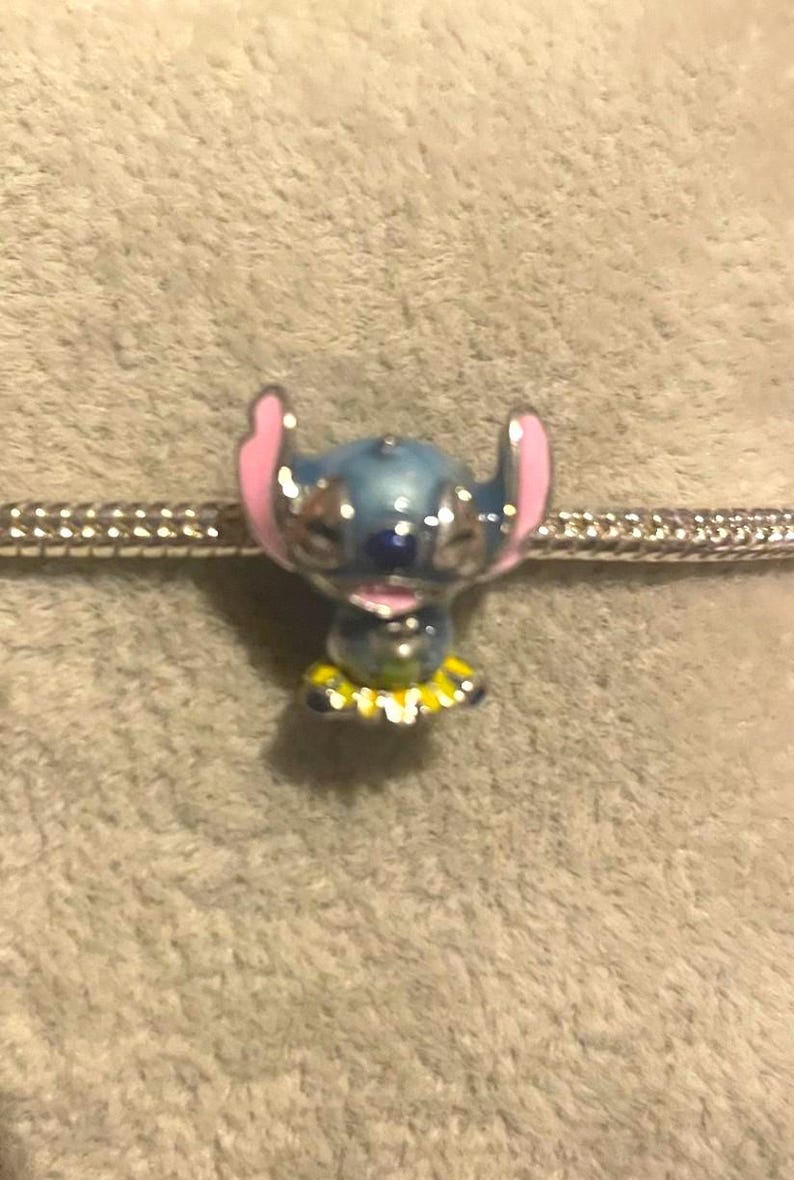 May include: A blue and pink Stitch charm bead with a yellow and white collar on a silver bracelet. This charm is a collectible item, ideal for fans of the animated movie.