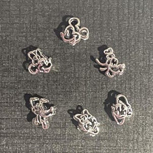 May include: Six silver-colored charms in various Mickey Mouse designs. The charms are arranged on a dark gray surface. The designs include Mickey Mouse, Minnie Mouse, and other related characters. These charms are suitable for jewelry making or crafting.