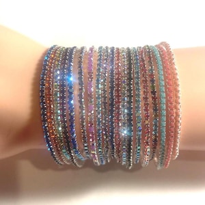 May include: A collection of colorful rhinestone bracelets. The bracelets are in various colors, including blue, orange, pink, and green. The bracelets are stacked on a wrist, creating a sparkling and eye-catching display.