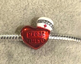 May include: A red heart-shaped charm with the words "great nurse" in cursive. The charm has a white nurse's cap with a red cross and rhinestone accents. The charm is on a silver bracelet.