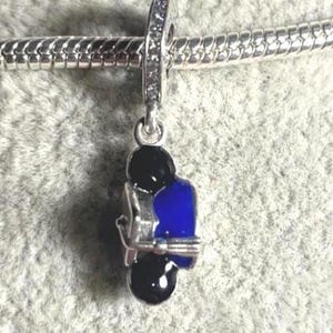 May include: A silver charm with a blue and black motorcycle design. The charm is suspended from a silver bracelet. The charm has a small loop at the top, encrusted with clear stones.
