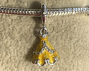 May include: A silver charm featuring a yellow dress pendant. The dress is decorated with silver-coloured accents and clear crystals. The charm is attached to a silver bracelet.