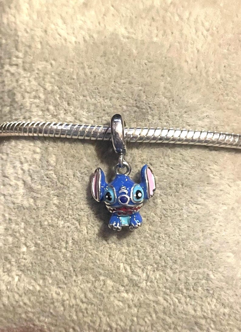 Puede incluir: Un charm de esmalte azul y rosa con el personaje Stitch de la pel&iacute;cula de Disney Lilo & Stitch. El charm est&aacute; suspendido de una pulsera de metal plateado. El charm tiene orejas grandes y una cara detallada.