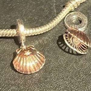 May include: Two silver charm bracelets with a seashell charm. The seashell charm is open and has a star design inside. The other charm is closed and has a detailed design.