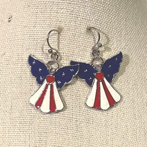 K&ouml;nnte beinhalten: Ein Paar patriotische Engels-Ohrringe. Jeder Ohrring hat blaue Fl&uuml;gel mit wei&szlig;en Sternen, ein rotes Herz und ein wei&szlig;-rot gestreiftes Kleid. Die Ohrringe haben silberfarbene Haken.