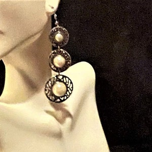 May include: Silver tone dangle earrings with three round, openwork, filigree circles. Each circle has a white pearl in the center.