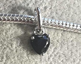 May include: A silver-toned charm with a black heart-shaped gemstone. The charm is suspended from a silver chain. The gemstone has a faceted surface and is accented with small silver details.