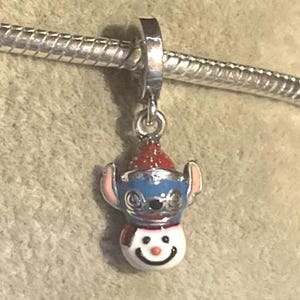Puede incluir: Un charm de plata con un personaje azul y blanco con un gorro y bufanda rojos, que se asemeja a un mu&ntilde;eco de nieve. El charm est&aacute; unido a una pulsera de plata. El personaje tiene orejas rosas y una cara sonriente.