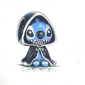 May include: A blue character with large eyes and a mischievous grin, wearing a black hooded cloak with silver trim. The figure has a small body and is standing on a white surface. The character is a stylized representation of Stitch.