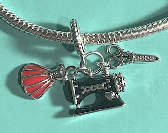 May include: A silver charm bracelet with a black sewing machine charm, a red fabric flower charm, and a silver pair of scissors charm.