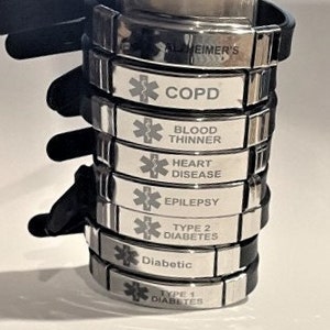 May include: A stack of silver medical alert bracelets with black bands. The bracelets are engraved with the Star of Life symbol and various medical conditions, including COPD, Blood Thinner, Heart Disease, Epilepsy, Type 2 Diabetes, Diabetic, and Type 1 Diabetes.