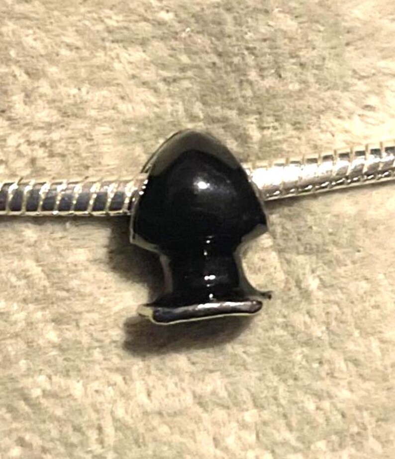 May include: A black, glossy charm bead with a rounded top and a flared base. The bead is attached to a silver-colored, snake chain bracelet. The charm has a smooth, polished finish.