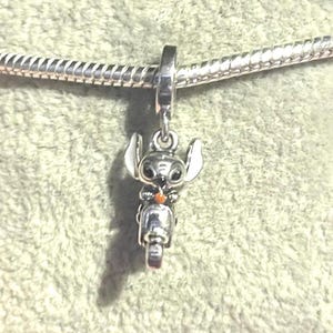 Puede incluir: Un charm de plata con el personaje Stitch de Lilo & Stitch en una scooter. El charm tiene detalles blancos y negros en las orejas y los ojos, y un acento naranja. Cuelga de una cadena de plata.