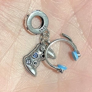 May include: A silver charm with a gaming theme. The charm features a controller with blue and clear accents, and a headset with blue earcups. The charm is marked with "S925" and has a star pattern around the top.