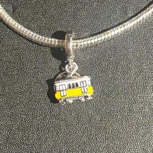 May include: A silver charm in the shape of a yellow trolley car. The charm is attached to a silver chain.