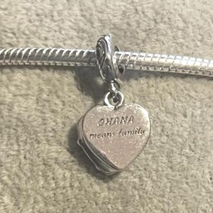May include: A silver charm with a heart-shaped pendant. The pendant has the words "OHANA means family" engraved on it. The charm is attached to a silver bracelet.