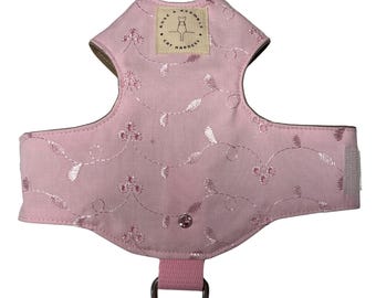 May include: A pink cat harness with embroidered floral detailing. The harness features a D-ring for leash attachment and a small tag with the text "Rose & Bramble Cat Harnesses". The harness has a velcro closure.
