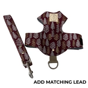 Peut inclure: Un harnais pour animaux de compagnie bordeaux et un ensemble de laisse assortie. L'ensemble présente un motif répété de motifs de feuilles blanches et dorées. Le harnais a un anneau en D pour l'attache de la laisse et une petite étiquette. Le texte "ADD MATCHING LEAD" est en bas.
