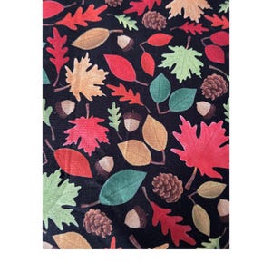 May include: A black fabric featuring a repeating autumn-themed pattern of colorful leaves in shades of red, orange, yellow, and green, interspersed with brown pinecones and small acorns. The design covers the entire surface of the material.