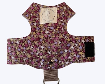 May include: A burgundy cat harness with a repeating pattern of gold, white, and purple stars and swirls. The harness has a brown strap with a metal D-ring and a velcro closure. A small label reads "Rose & Bramble Cat Harness".