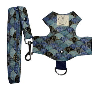 Puede incluir: Un arnés para gato y correa a juego con un patrón de ondas en forma de abanico en azul, azul claro y negro con detalles dorados. El arnés incluye una etiqueta de tela color crema con el texto Rose & Bramble Cat Harness.