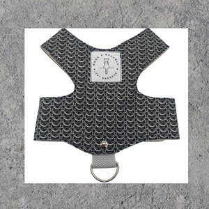 Puede incluir: Arnés para gatos con un diseño de cota de malla en tonos grises y negros. Tiene un anillo en D para la correa y una etiqueta con el texto "Rose & Bramble Cat Harness". El arnés está diseñado para adaptarse al pecho y los hombros del gato.