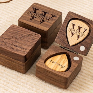 May include: Three wooden boxes with personalized engravings. One box features a guitar silhouette with the name "Garrett" engraved on it. Another box has a guitar pick with the letter "W" and the name "Winston" engraved on it. The third box has the letter "W" and the name "Winston" engraved on it.