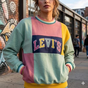 May include: A color-block sweatshirt with the Levi's logo. The sweatshirt features panels of pink, green, and yellow. The Levi's logo is in a navy blue rectangle with yellow and pink lettering. The cuffs and neckline have striped detailing.