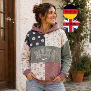 May include: A patchwork hoodie featuring a mix of floral and daisy patterns in shades of mauve, sage green, and dark gray. The center panel is sage green with the word NIKE in white block letters and a white swoosh logo underneath the text.