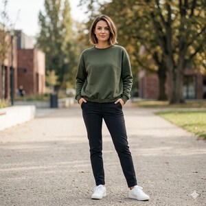 Pode incluir: Uma mulher vestindo um moletom verde-oliva com cintura ajustada, cal&ccedil;as pretas e t&ecirc;nis brancos. A roupa &eacute; casual e adequada para atividades ao ar livre. O fundo apresenta uma passarela pavimentada e &aacute;rvores.