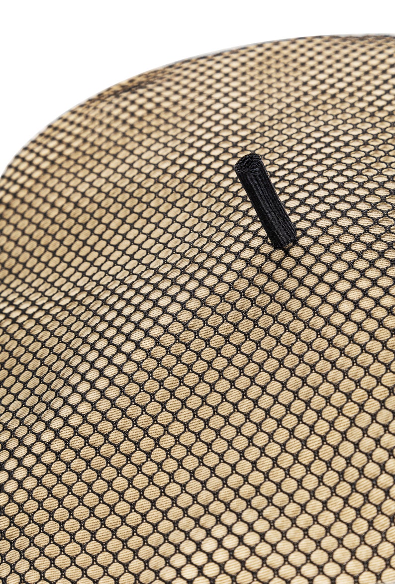 May include: A close-up of a beige mesh fabric with a black strap. The fabric has a grid pattern.