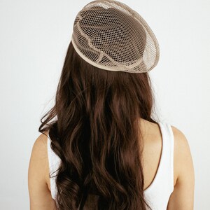 May include: A woman with long brown hair is wearing a beige mesh hat. The hat is round and has a wide brim.
