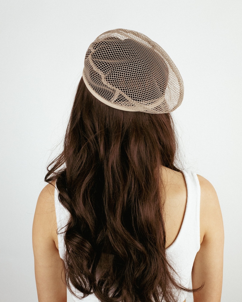 May include: A woman with long brown hair is wearing a beige mesh hat. The hat is round and has a wide brim.