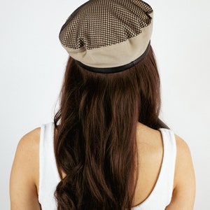 May include: A beige beret with a black mesh panel on top. The beret has a black band around the bottom.