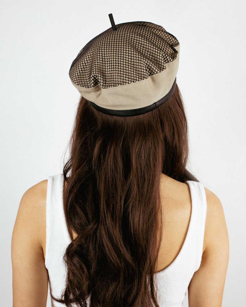 May include: A beige beret with a black mesh panel on top. The beret has a black band around the bottom.