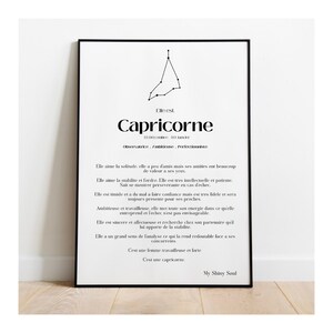 May include: A framed black and white print featuring the Capricorn zodiac sign. The print includes the Capricorn symbol, dates, and descriptive text in French. The artwork is displayed on a white wall.