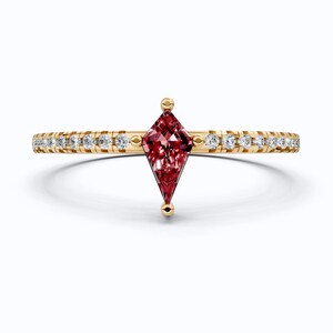 May include: A gold ring with a kite-shaped, deep red gemstone at its centre. The band is embellished with small, sparkling white gemstones. The ring has a delicate, elegant design, suitable for a special occasion.