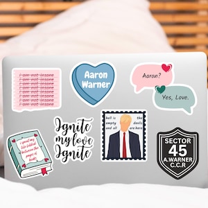 May include: A laptop computer with several stickers on it. The stickers are various colors and feature text and images. The text on the stickers includes "I am not insane", "Aaron Warner", "Ignite my love Ignite", "hell is empty and all", "the devils are here", "Aaron?", "Yes, Love", "SECTOR 45 A.WARNER C.C.R."
