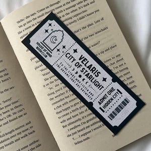 May include: Black bookmark with white text and stars. The bookmark features the text "House of Wind Bookclub", "Velaris City of Starlight", "To the stars who listen and the dreams that are answered", and "Admit One Hidden City".