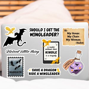 May include: A laptop computer with several stickers on it. The stickers feature dragons, a quote about reading, and a bottle of potion. The text on the stickers reads "Should I get the Wingleader?", "Violent little thing", "Save a dragon ride a wingleader", "A reader without their Kindle is a tragedy", "Basgiath War College", "Violence Apothecary", and "Vi- My House. My Chair. My Woman. -Xaden".