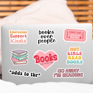 May include: A laptop computer with several colorful stickers featuring book-themed sayings. The stickers include "Emotional Support Kindle", "Books over People", "Books keep reality away", "Hot Girls Read Books", "Go Away I'm Reading", and "Admit One Anti-Social Book Lover".