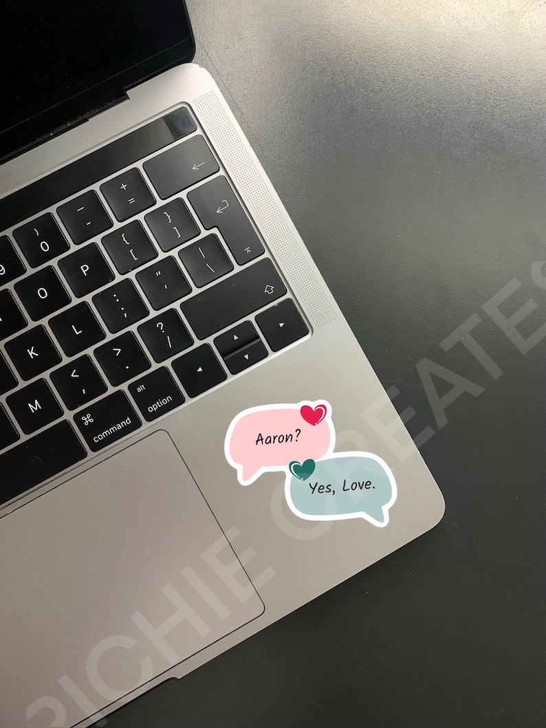 May include: A laptop computer with a pink and blue speech bubble sticker with the text "Aaron?" and "Yes, Love."