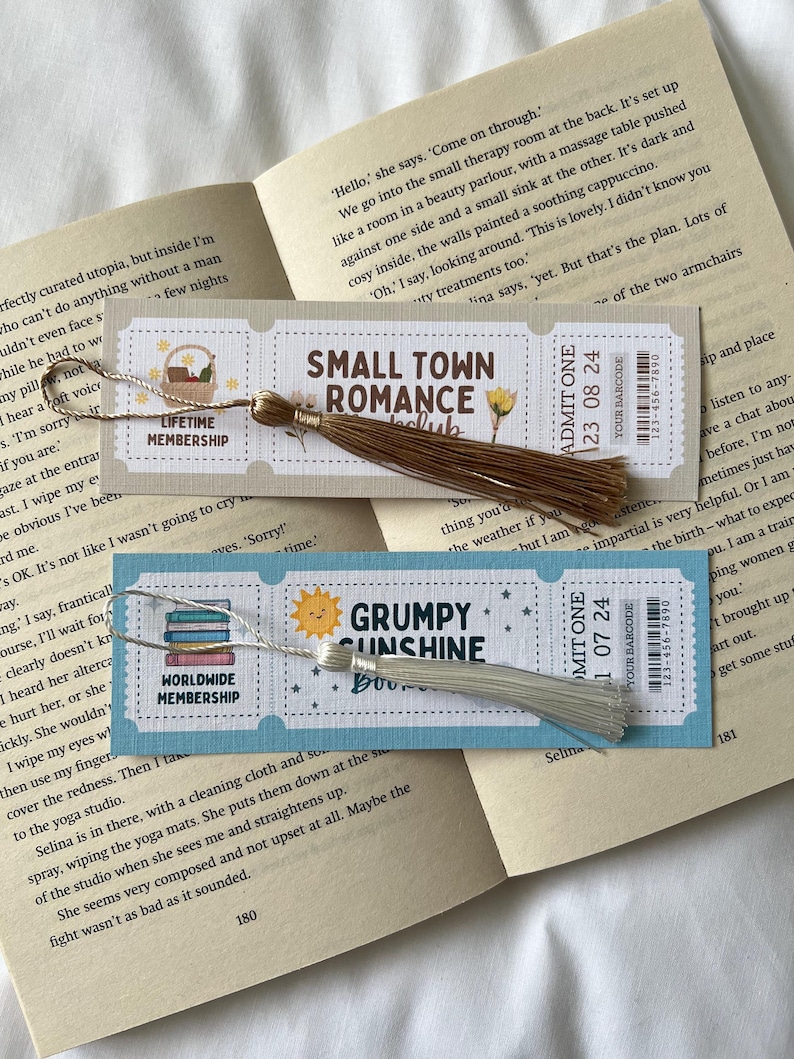 May include: Three different bookmark designs with tassels. The bookmarks feature illustrations of a book stack, a sun, and a flower. The text on the bookmarks reads "Lifetime Membership", "Worldwide Membership", "Small Town Romance", "Grumpy Sunshine", "Admit One 23 08 24", and "Admit One 1 07 24".