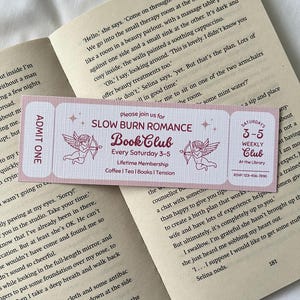 May include: A pink and white ticket with the text "Slow Burn Romance Book Club" in red. The ticket has a graphic of two cherubs with arrows. The text "Every Saturday 3-5" is below the title. The text "Lifetime Membership" is below that. The text "Coffee | Tea | Books | Tension" is below that. The ticket is for a book club.