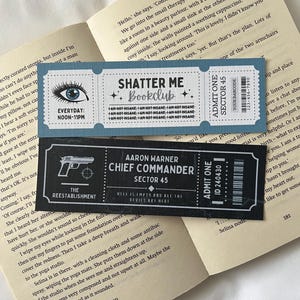 Peut inclure: Deux signets bleus et noirs sur le thème d'un club de lecture. Le signet du haut présente un œil bleu avec le texte "Shatter Me Bookclub" et le texte "Je ne suis pas fou" répété plusieurs fois. Le signet du bas présente une illustration en noir et blanc d'un pistolet avec le texte "The Reestablishment" et le texte "Aaron Warner Chief Commander Sector 45" avec le texte "L'enfer est vide et tous les diables sont ici".