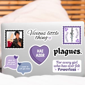 May include: A laptop with several stickers on it. The stickers are purple and feature quotes from the book "Vicious" by V.E. Schwab. The quotes include "Vicious little thing", "Kai Azer", "Hunted Hunter", "plagues", and "For every girl who has ever felt +Powerless+".