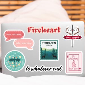 May include: A laptop covered in various stickers. The stickers include text that says "Fireheart", "hello, witchling", "hello, princeling", "TERRASEN - ERILEA", "THE THIRTEEN", "you do not yield", "to whatever end", and "fire breathing bitch queen".