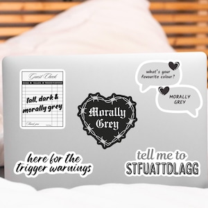 May include: A collection of black and white stickers with various phrases and designs. One sticker resembles a guest check with the text "tall, dark & morally grey." Other stickers include a heart with barbed wire and the words "Morally Grey."