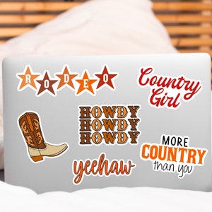 May include: A laptop computer with several stickers on it. The stickers are in various colours and feature the words "Rodeo", "Howdy", "Yeehaw", "Country Girl", and "More Country than you".